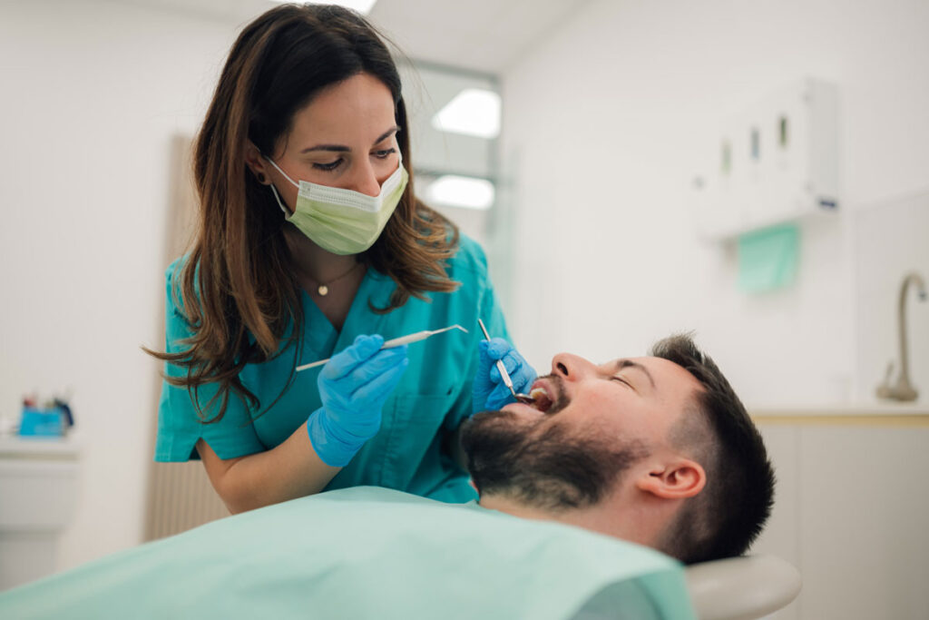 femeie dentist care examineaza cu instumente medicale dintii pacientului
