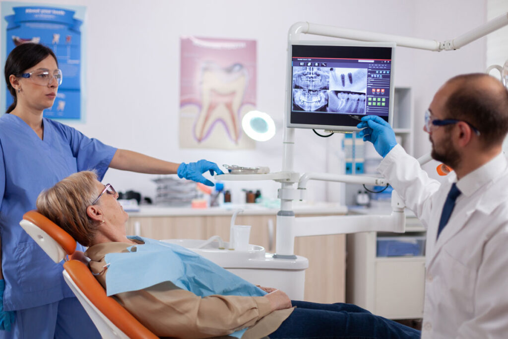 medic stomatolog care explica pacientei, pe un monitorul riscurile implantului dentar